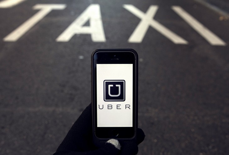 The logo of car-sharing service app Uber on a smartphone over a reserved lane for taxis in a street is seen in this photo illustration taken in Madrid on December 10, 2014. A Madrid judge has ordered U.S.-based online car booking company Uber to cease operations in Spain, the latest ban on the popular service. Taxi drivers around the world consider Uber unfairly bypasses local licensing and safety regulations by using the internet to put drivers in touch with passengers. REUTERS/Sergio Perez (SPAIN - Tags: LAW TRANSPORT SCIENCE TECHNOLOGY BUSINESS TELECOMS LOGO)